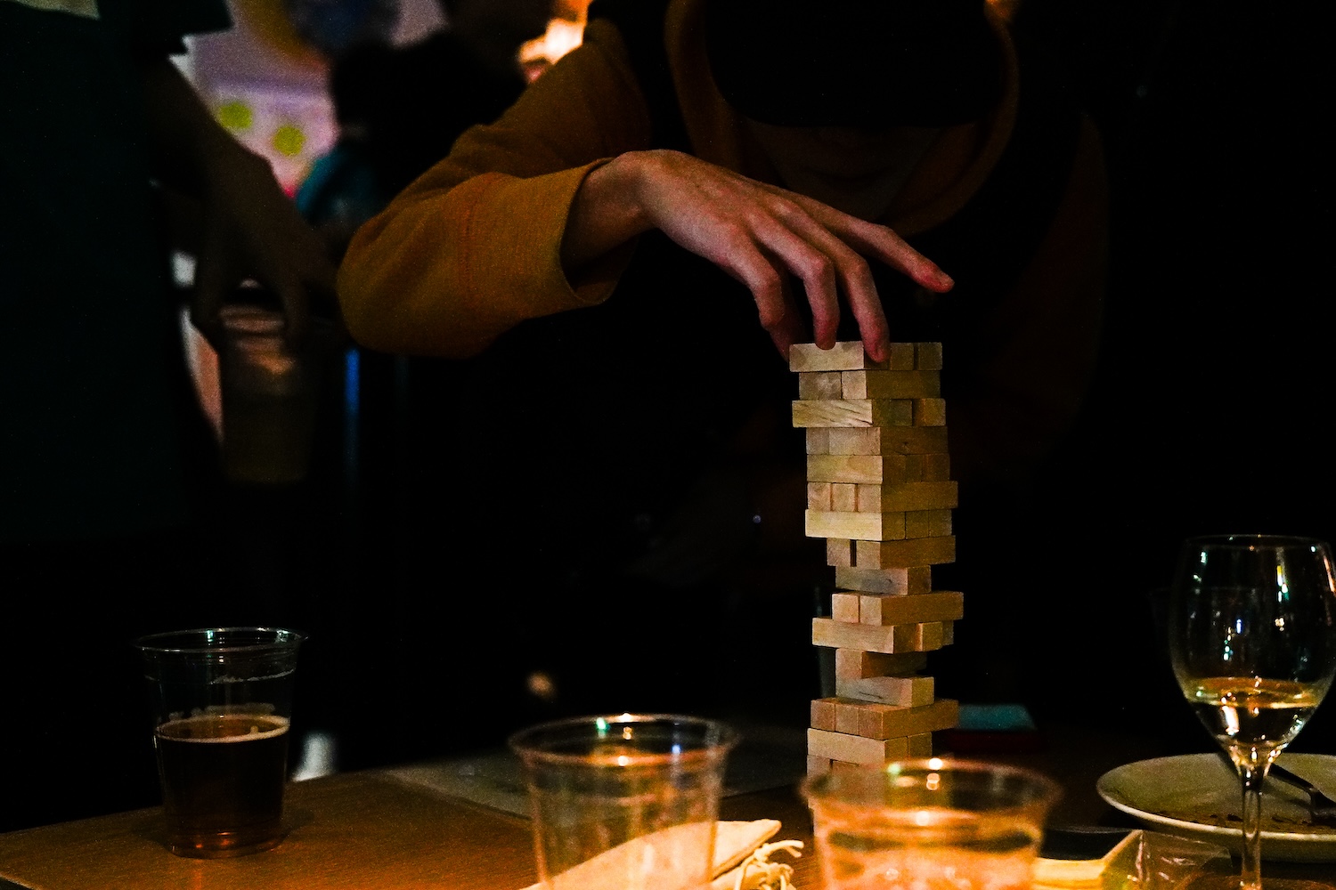 写真：パーティーでジェンガを楽しむ様子。テーブルには飲み物の入ったグラスやカップが並び楽しげな雰囲気の中、崩れそうな際どいジェンガの状態で、ゲームに集中している様子が見られる。